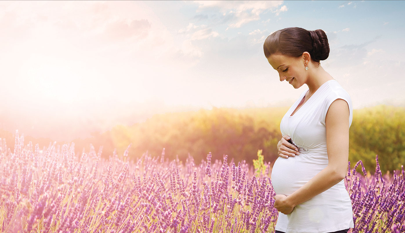 a pregnant woman dressed in white by flowers in a field