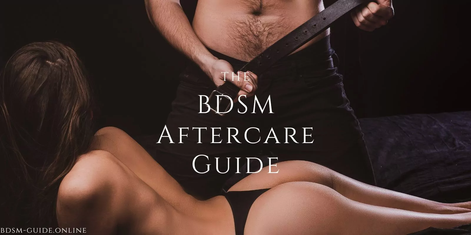 Man holding a leather belt standing behind a woman lying on her front, emphasizing a BDSM-themed dynamic.